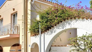 Un bâtiment doté d’un balcon, d’un mur blanc orné d’une arche décorative et de plantes grimpantes en fleurs.