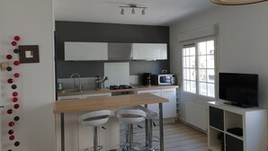 A modern kitchen with a central island, bar stools, a microwave, and a TV on a stand. - Apartment/ flat - Saint-Malo (Saint-Malo)