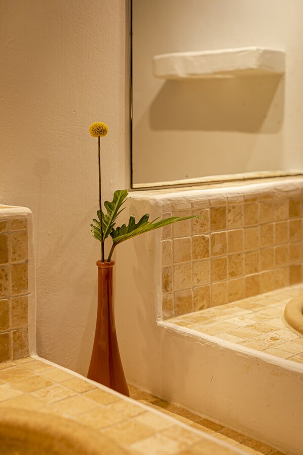 A bathroom with a tiled wall, a window, and a plant in a vase.