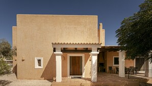 A building with a beige exterior, a wooden door, and a covered patio area with chairs. - CAN NOVES-Villa with terrace and BBQ in a central and quiet area (Sant Francesc de Formentera)
