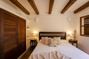 A bedroom with a large bed, wooden headboard, two bedside tables with lamps, and a wooden wardrobe.
