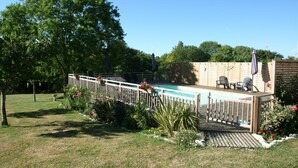A backyard with a wooden deck, a swimming pool, and a patio area with chairs and an umbrella. - Walnut Lodge, 1 bedroom traditional Gite in rural location  (Pleumartin)