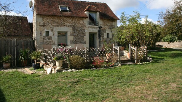 A stone house with a tiled roof, a small balcony, and a fenced garden with various plants and a wooden deck. - Walnut Lodge, 1 bedroom traditional Gite in rural location  (Pleumartin)