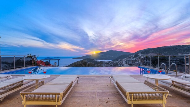 A rooftop infinity pool with lounge chairs and a sunset view.