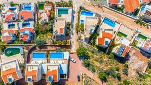 An aerial view of a residential area with multiple houses, each featuring a swimming pool and a red-tiled roof.