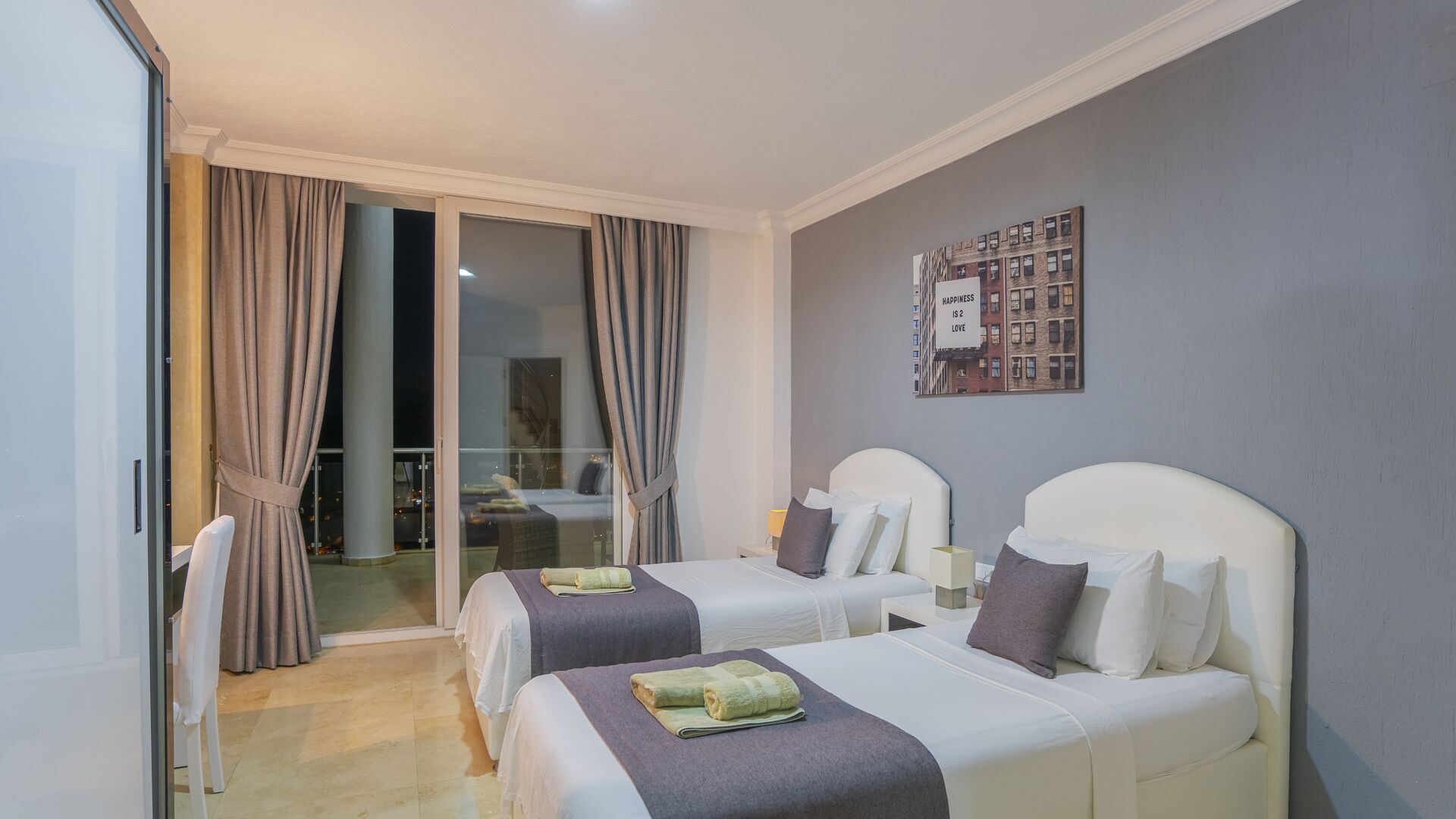 A hotel room with two beds, a sliding glass door to a balcony, and a cityscape view.