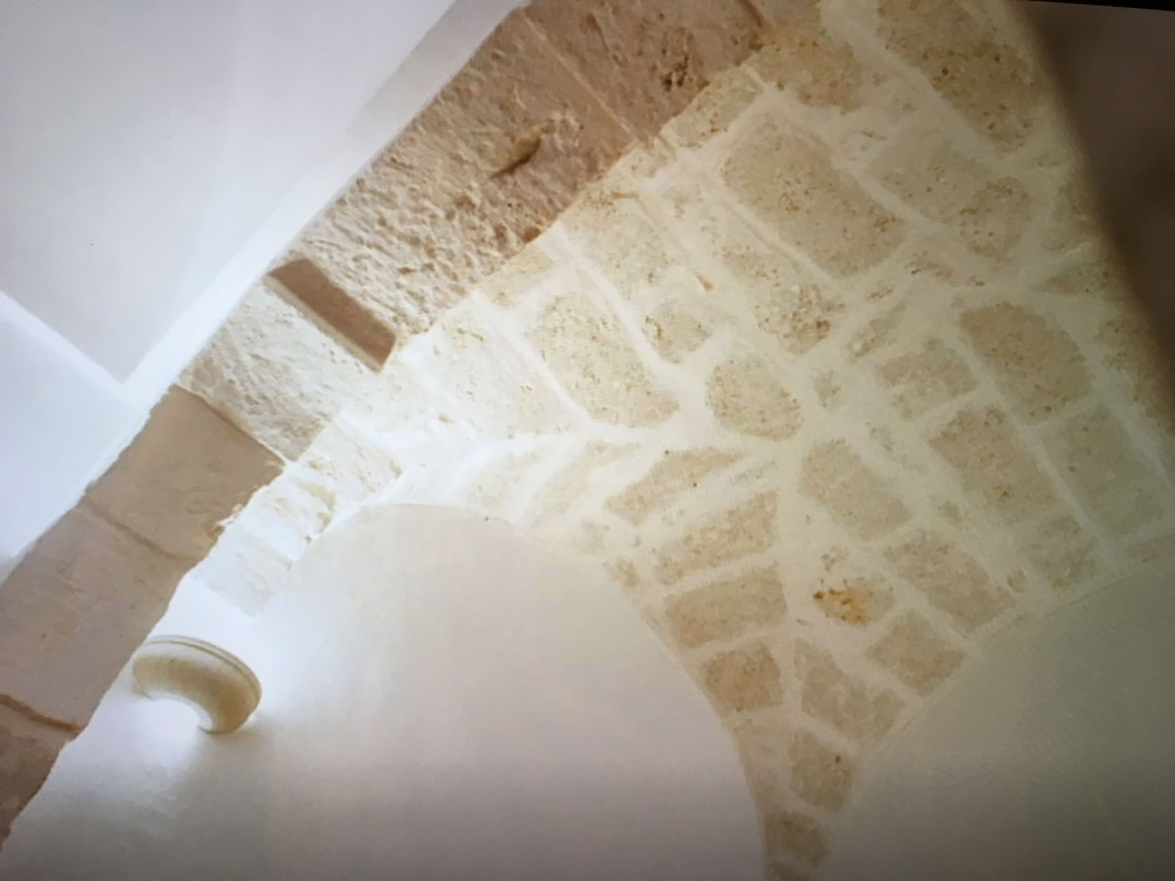 Pared de piedra con techo blanco y un objeto curvo blanco, posiblemente una silla o un mueble.