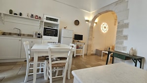 A modern kitchen with white cabinetry, a dining table with chairs, a built-in oven, and a stone archway. - Dimora Maria Chiara with panoramic terrace and sea view (ostuni)