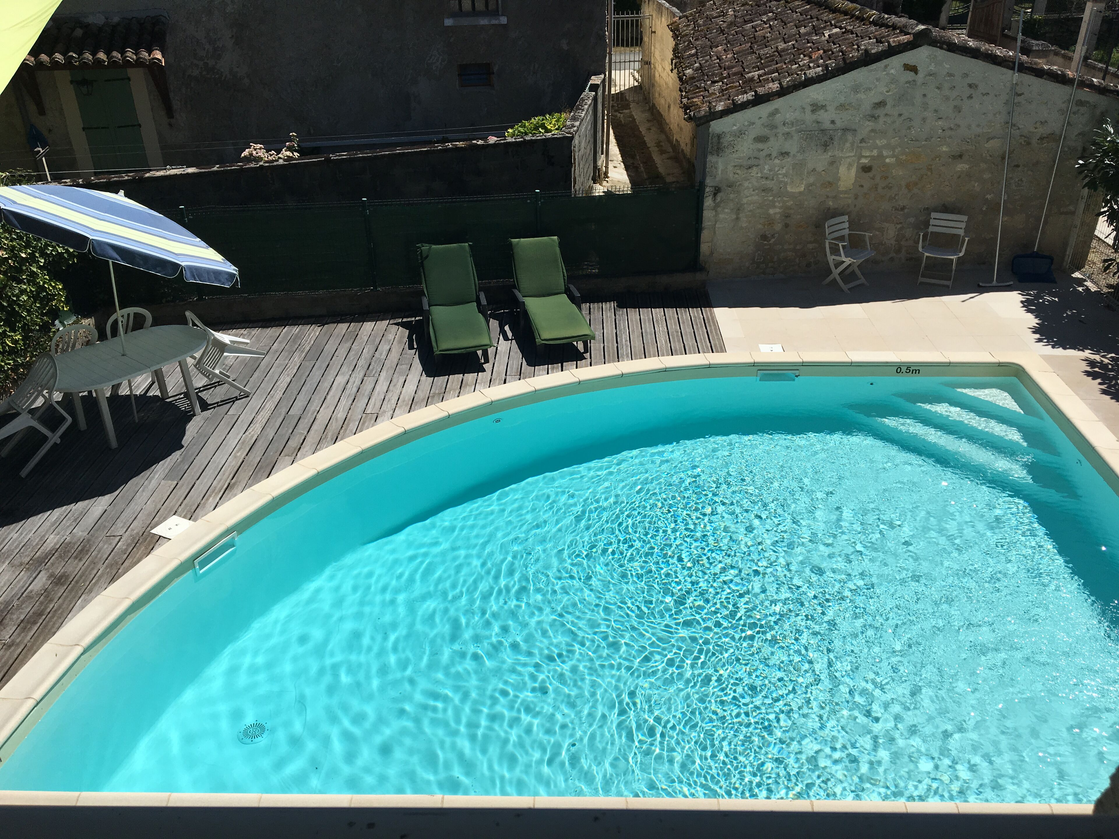 Une piscine aux eaux cristallines, dotée d’une terrasse en bois, de chaises longues vertes et d’une table avec des parasols.