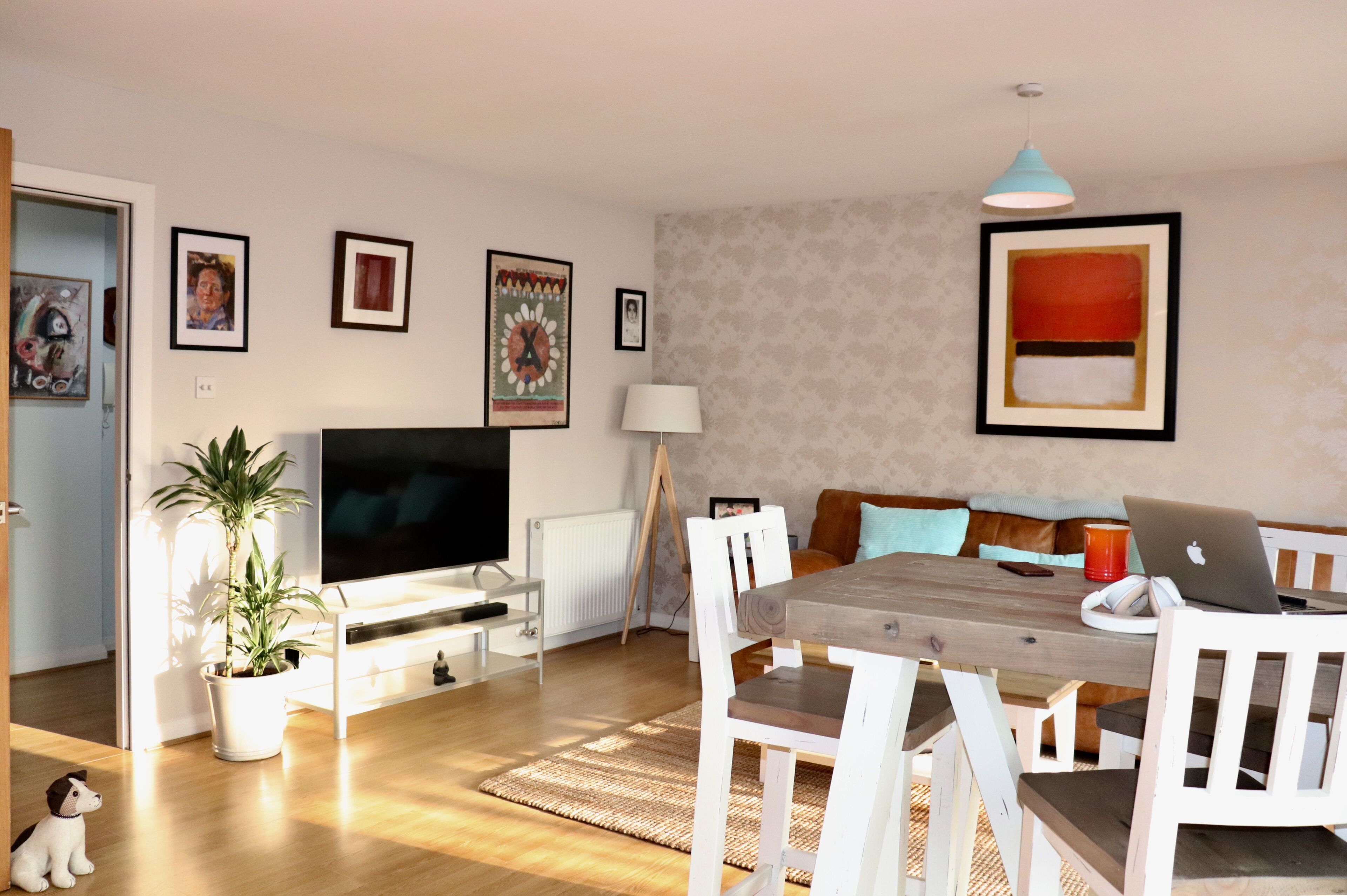 A living room with a TV, sofa, dining table, and chairs. There is a plant, a lamp, and artwork on the walls.