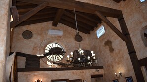A rustic interior with exposed wooden beams, a chandelier, and a circular window.