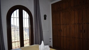 A hotel room with a bed, a large arched window, and a wooden wardrobe.