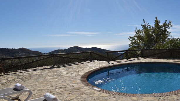A stone pool with a wooden deck, surrounded by a wooden railing, overlooking a mountainous landscape.
