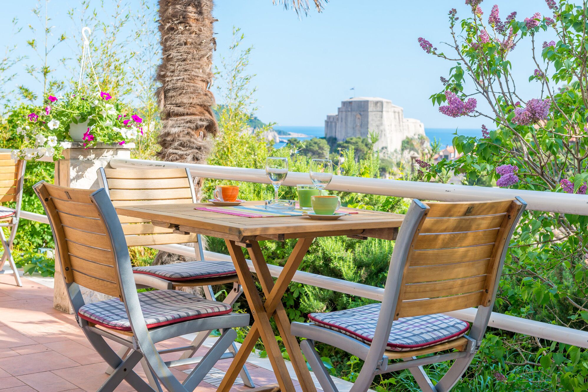Ein Holztisch mit zwei Stühlen, Blick auf das Meer und eine Palme.