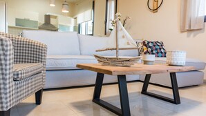 A modern living room with a checkered armchair, a wooden coffee table with a sailboat decoration, a grey sofa, and a white vase with a geometric pattern.