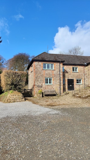 A stone building with a tiled roof, a gravel driveway, and a wooden bench.