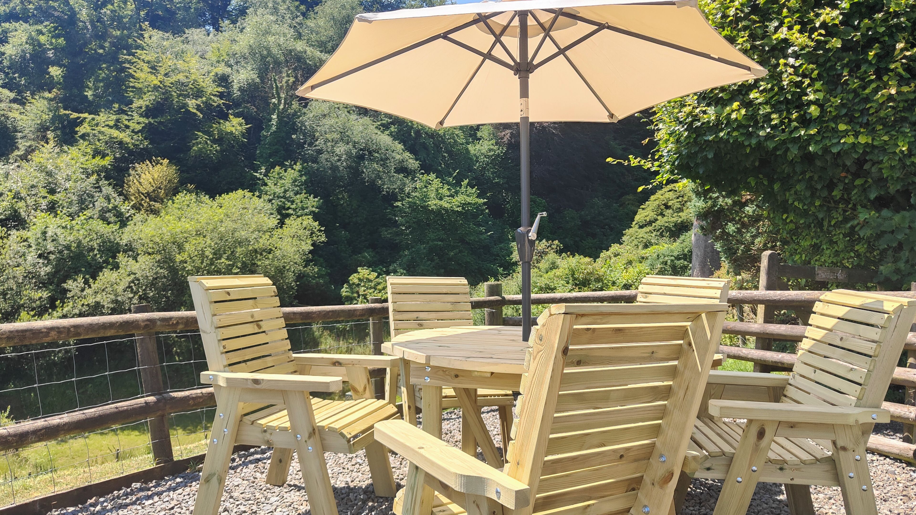 A wooden deck with a table and chairs, an umbrella, and a view of a forested area.