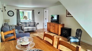 A living room with a sofa, TV, wooden cabinet, dining table with chairs, and a clock on the wall.