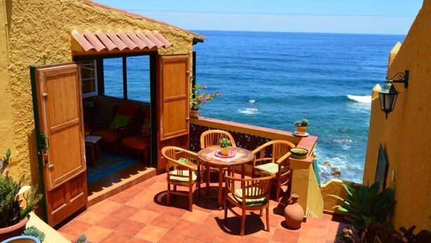 Un patio con una mesa y sillas, una puerta de madera y vista al océano.