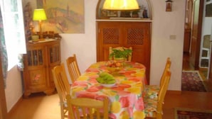 Un comedor con una mesa cubierta por un mantel estampado con motivos de frutas, rodeado de sillas de madera.