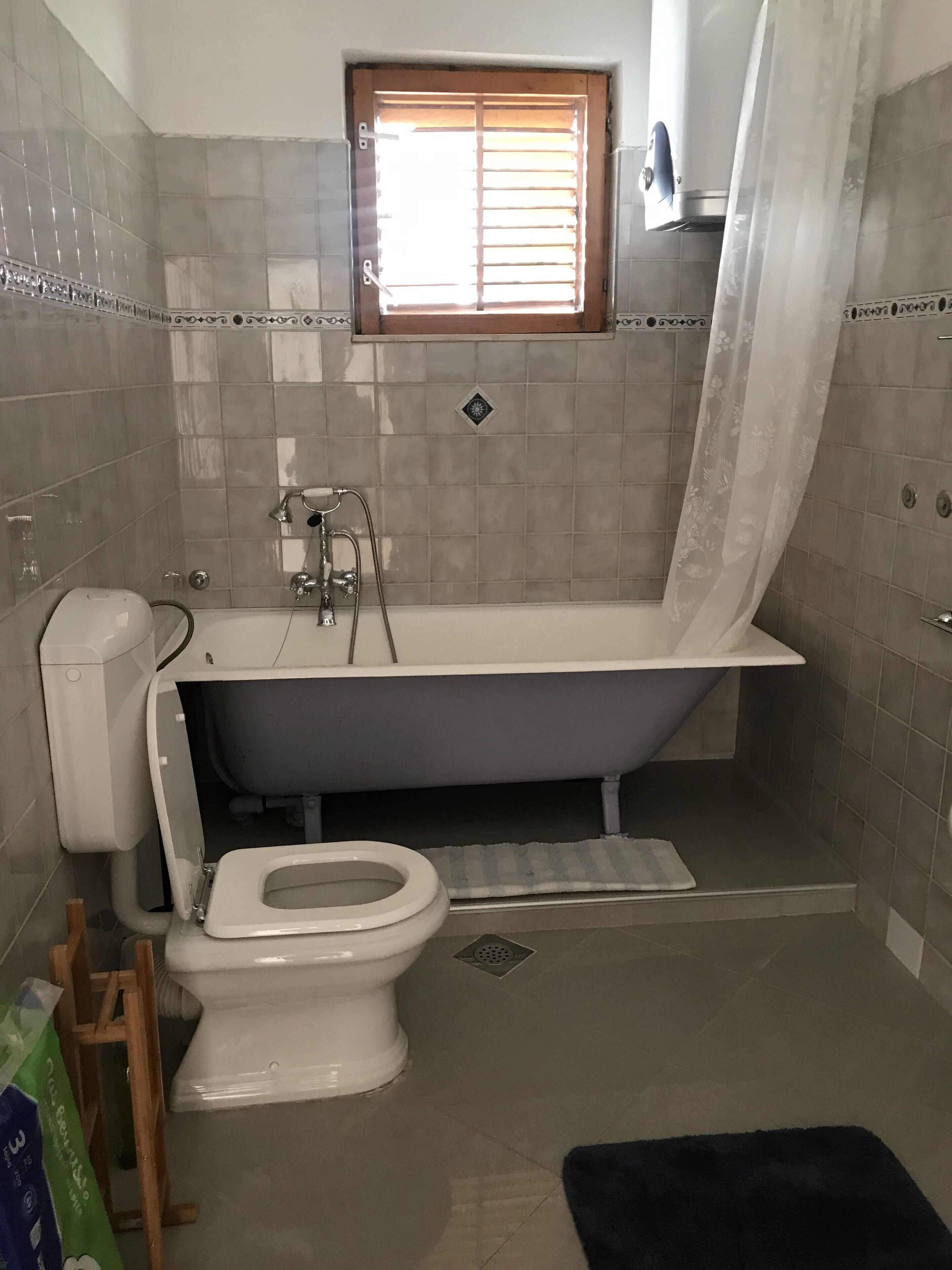 A bathroom with a bathtub, toilet, and a window with blinds.