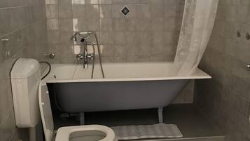 A bathroom with a bathtub, toilet, and a window with blinds.