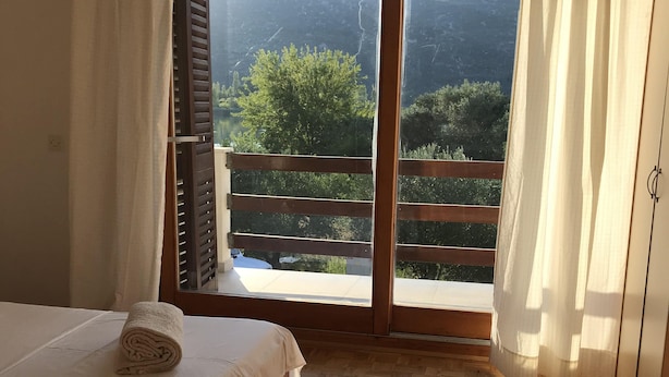 A bedroom with a wooden floor, a bed with a rolled towel, and a view of mountains through a large window with wooden shutters. - Holiday house " Katy" on Bacina Lakes (PLOCE, PERACKO BLATO)