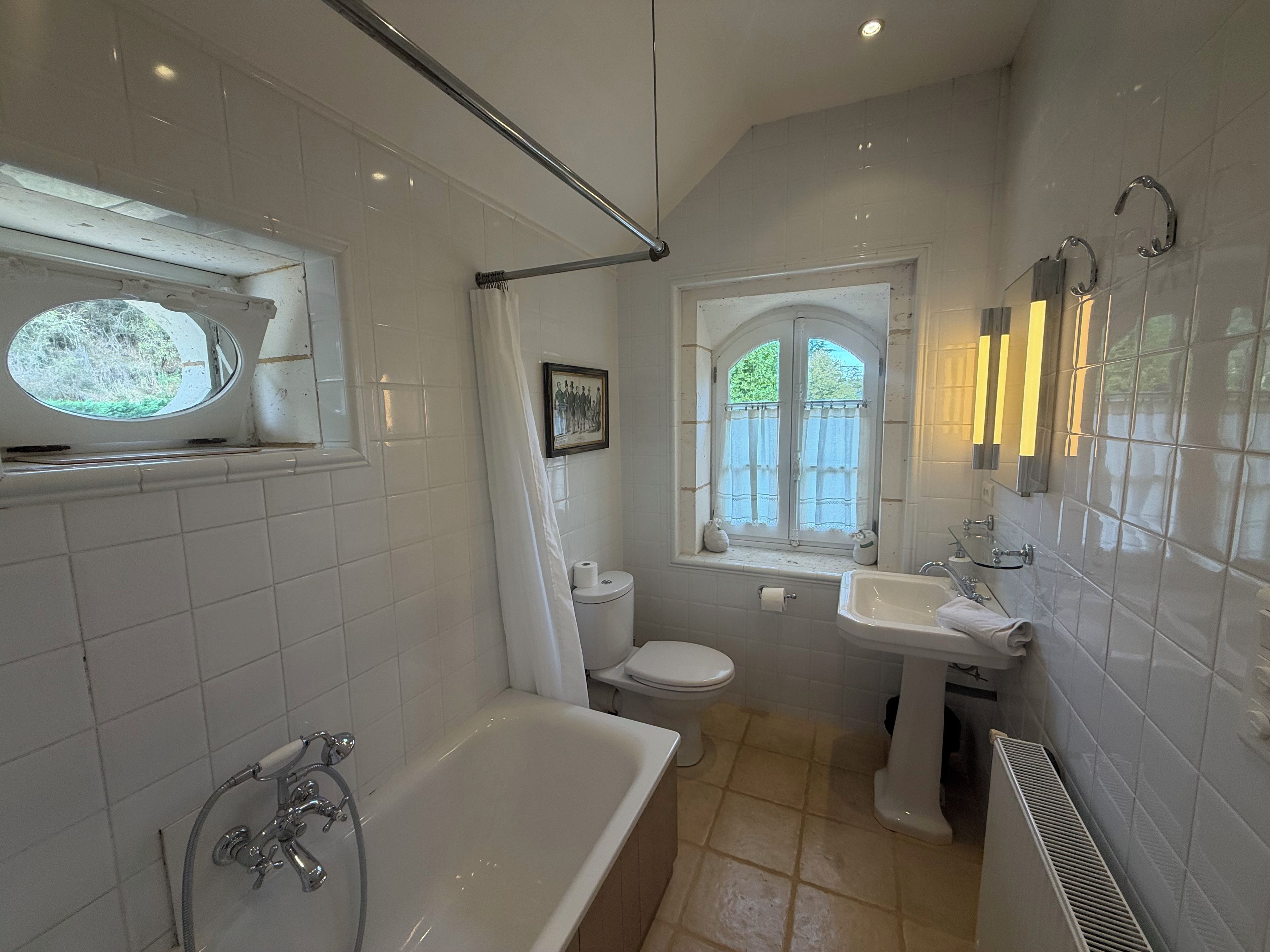 A bathroom with a bathtub, toilet, and sink, featuring white tiles and a window with a view.