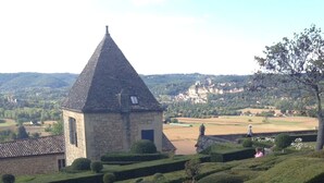 Un bâtiment en pierre surmonté d’un toit conique, entouré de haies parfaitement taillées et offrant une vue dégagée sur la campagne.