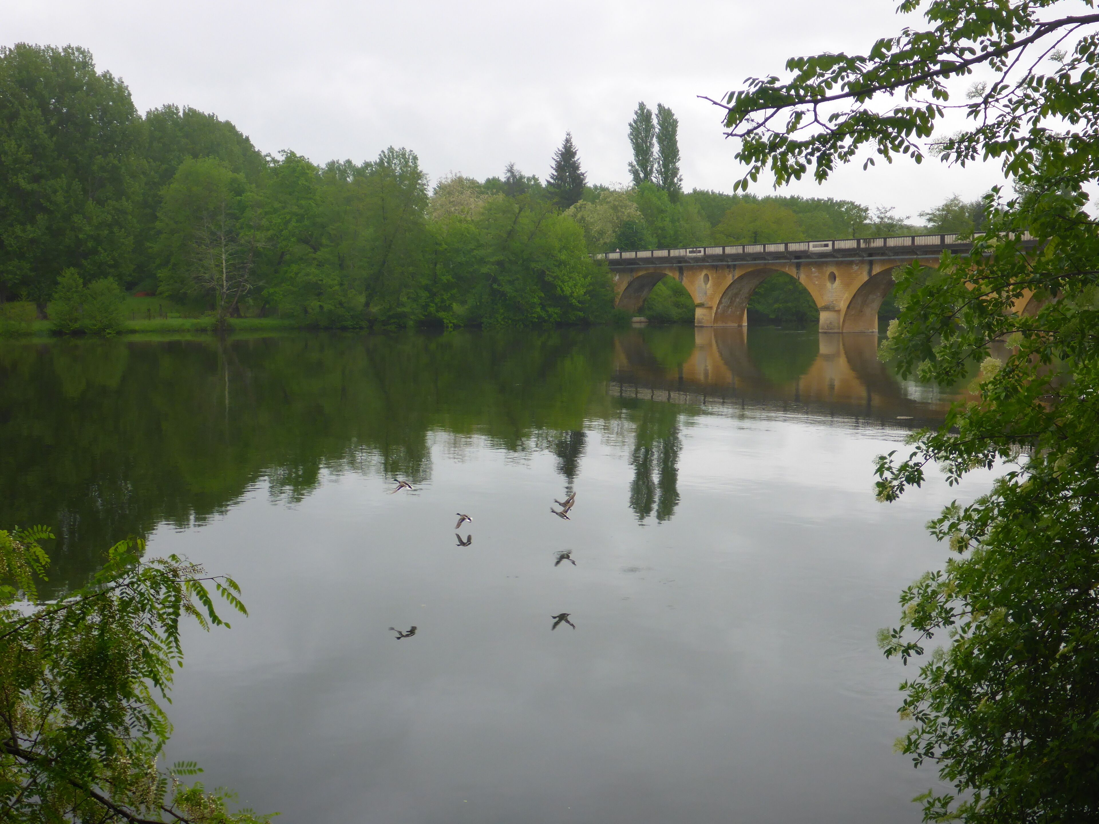 A bridge over a calm river with reflections of trees and the bridge structure.