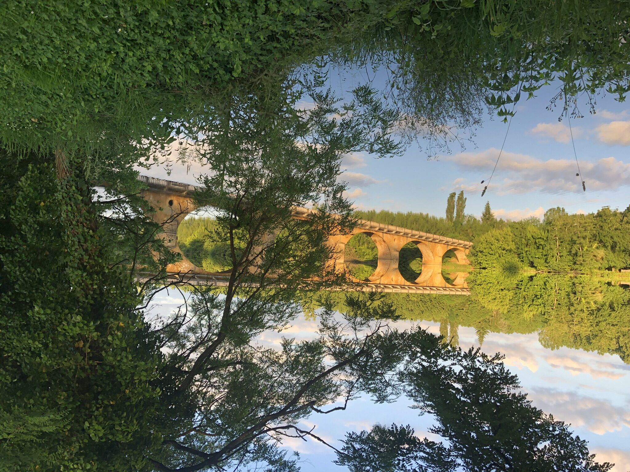 A bridge with multiple arches over a calm body of water, surrounded by dense greenery.