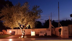 A swimming pool with a stone wall and a tree with lights. There are outdoor seating areas and a stone structure in the background. - magic and charm in a trullo  (Noci)
