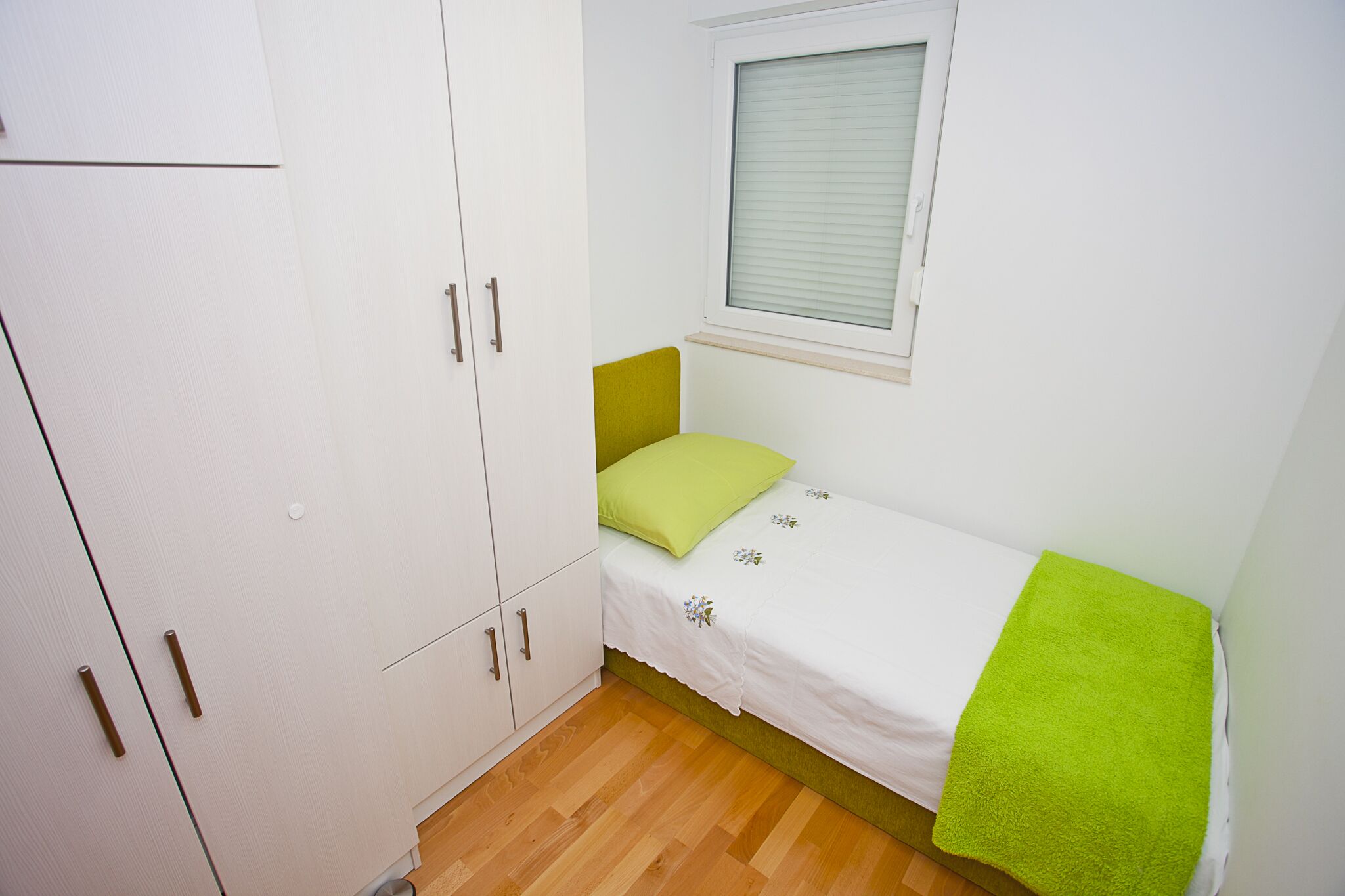 A small, single-bed room with a green pillow and a green towel on the bed.