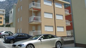 Un edificio residenziale a più piani con balconi, auto parcheggiate e montagne sullo sfondo.