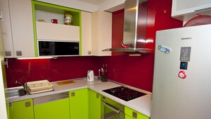 Cucina con mobili verdi, frigorifero in acciaio inossidabile e parete di fondo rossa.