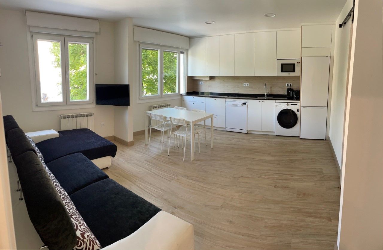 A modern kitchen with white cabinets, a dining table with chairs, and a built-in washing machine.