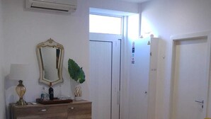 Ein Wohnzimmer mit Holzboden, einem weißen Sofa, einem Couchtisch mit Blumenvase, einem Spiegel und einer Kommode mit Lampe.