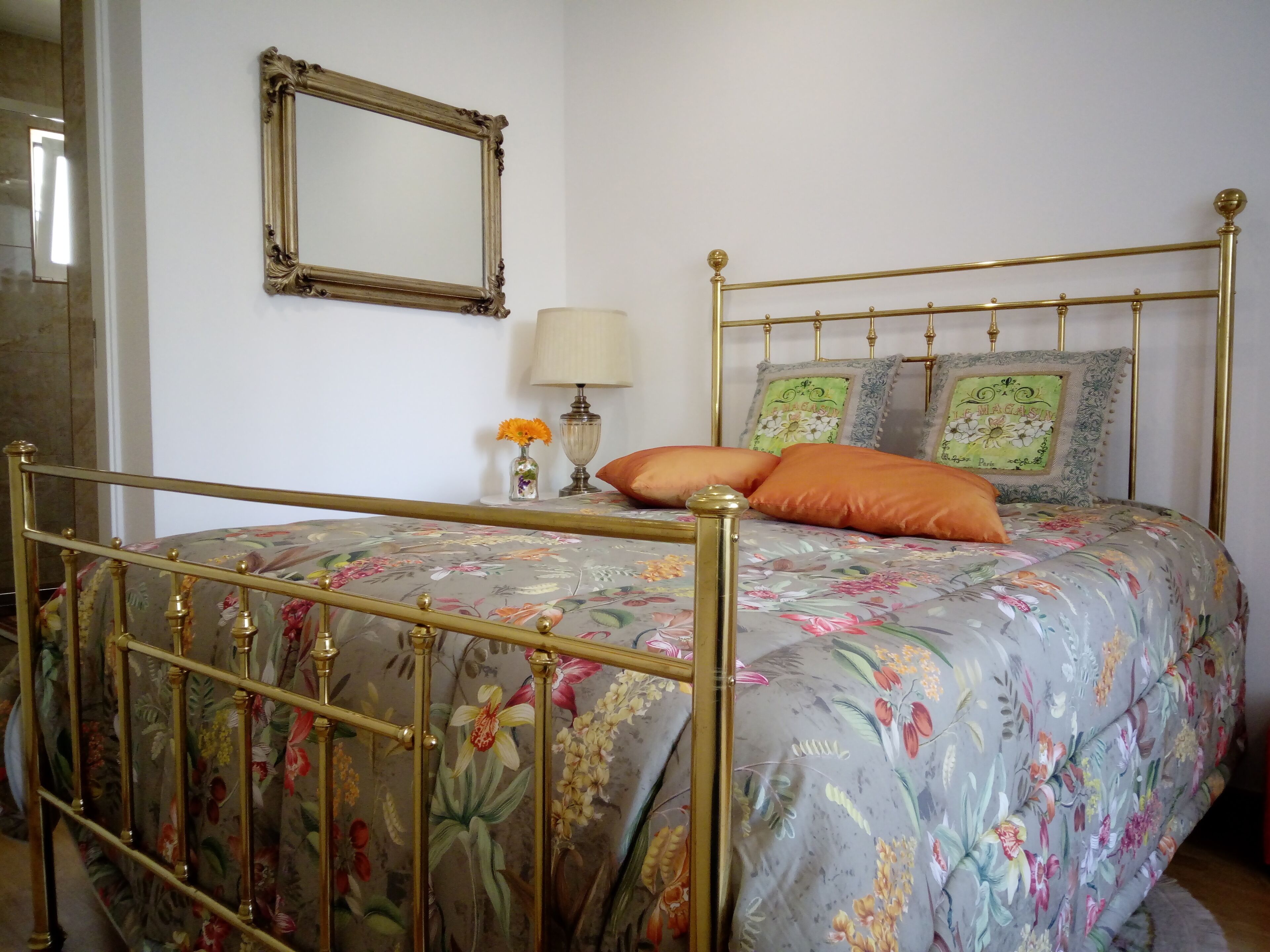Una cama con colcha estampada, cabecera con marco dorado y dos almohadones decorativos.