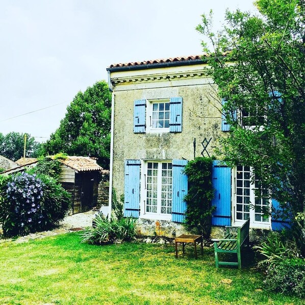 Une maison à deux étages avec des volets bleus, un petit porche et un jardin.