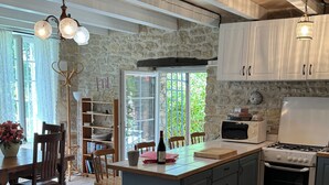 Une cuisine dotée d’un îlot central, de meubles blancs, d’un mur en pierre et d’un coin repas avec un canapé à motifs floraux.