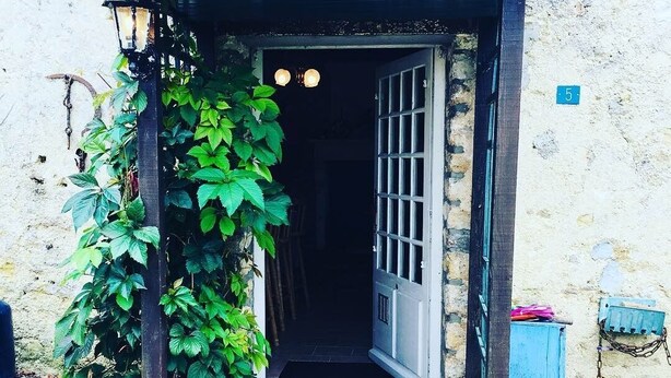 Une entrée rustique avec une porte en bois, un mur en pierre et un petit jardin agrémenté de feuillage verdoyant.