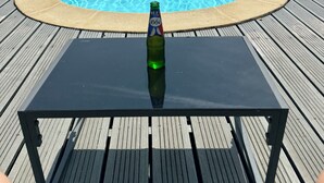 Une piscine avec une terrasse en bois et une table sur laquelle se trouve une bouteille, le tout en premier plan.