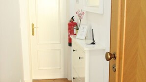 A narrow hallway with a doormat, a white cabinet with drawers, a small potted plant, and a door with a brass handle. - Sete Rios, Near Zoo Lisboa/ free Wifi (Lisboa)