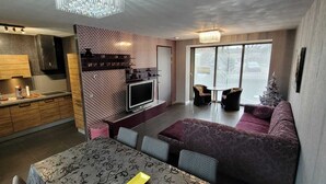 A modern kitchen with a built-in oven, a dining area with a patterned table, and a living space with a sofa and a Christmas tree.