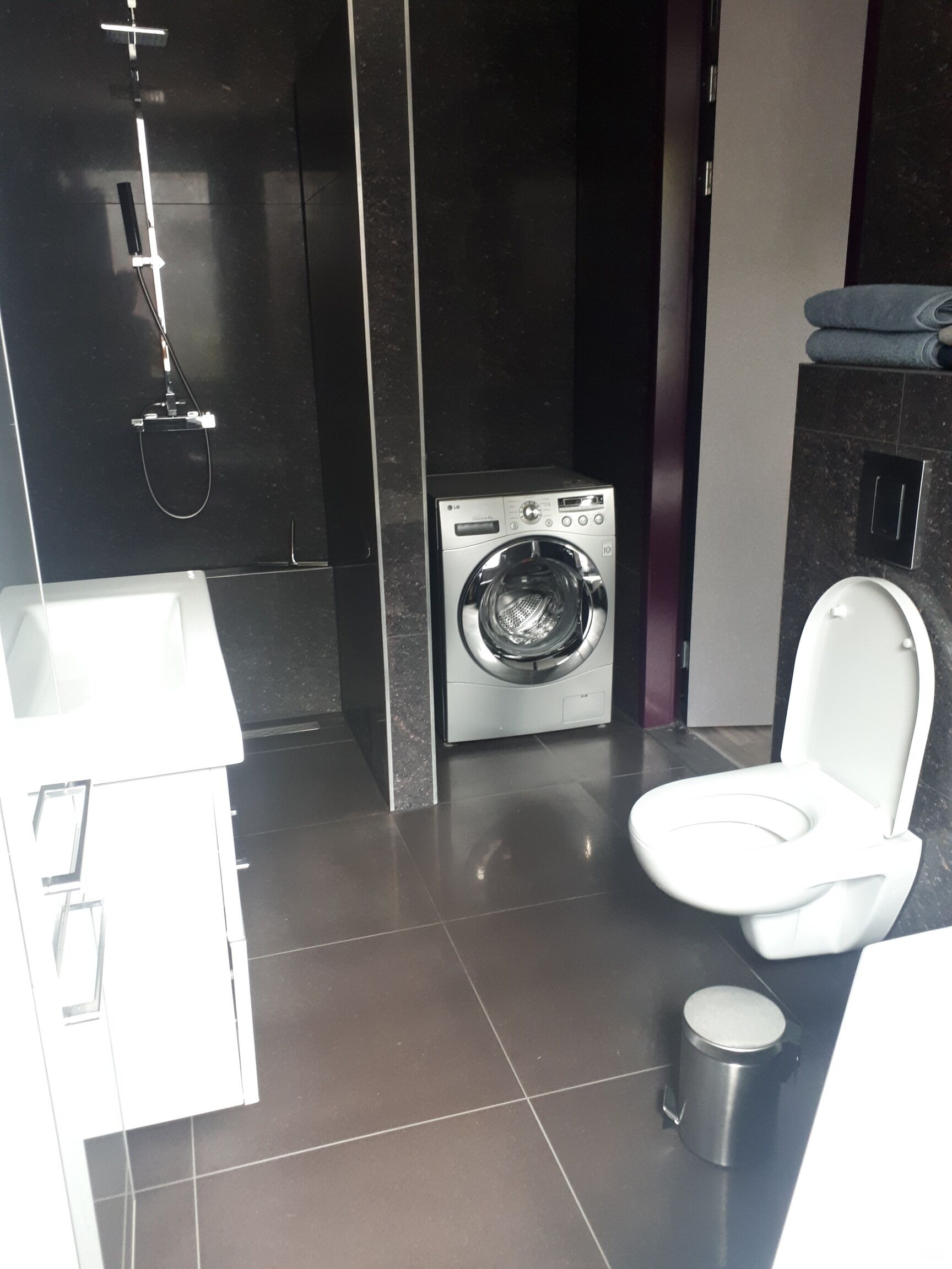 A compact bathroom with a washing machine, toilet, and sink.