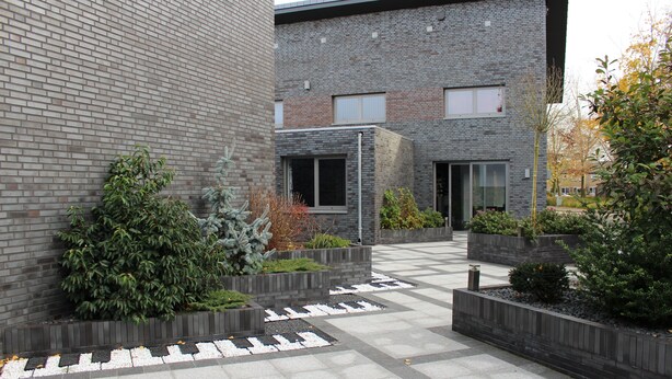 A modern building with a brick facade, outdoor seating areas with planters, and a paved courtyard.