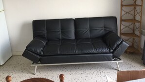 Un sofá de cuero negro con patas metálicas, una estantería escalonada de madera y un suelo moteado.