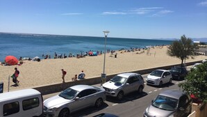 Una playa con coches aparcados al borde de la carretera y gente disfrutando de la arena y el mar.
