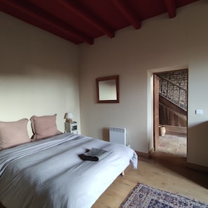 A bedroom with a bed, a nightstand, a lamp, a radiator, and a view of a stone staircase.