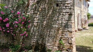 Un bâtiment en pierre à l’aspect rustique, entouré de verdure et de fleurs roses.